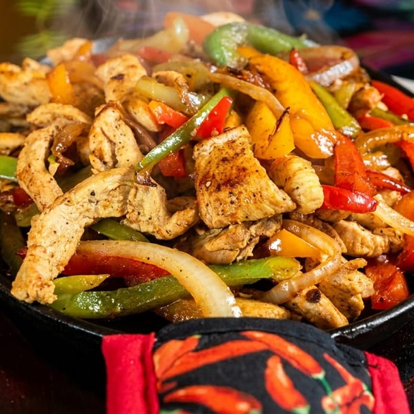 Sizzling chicken fajitas with colorful bell peppers and onions in a hot cast iron skillet.