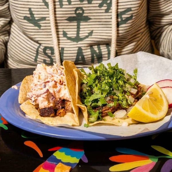 Two tacos, one with slaw and one with cilantro and onions, on a blue plate.