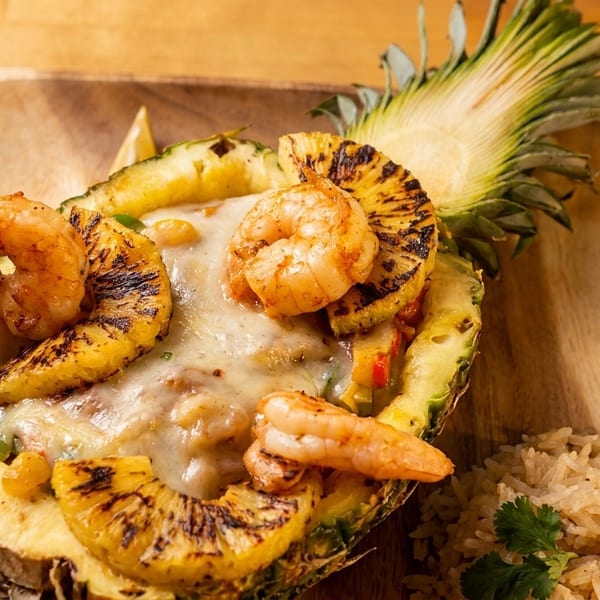 Grilled shrimp and pineapple served in a pineapple half with melted cheese and rice.