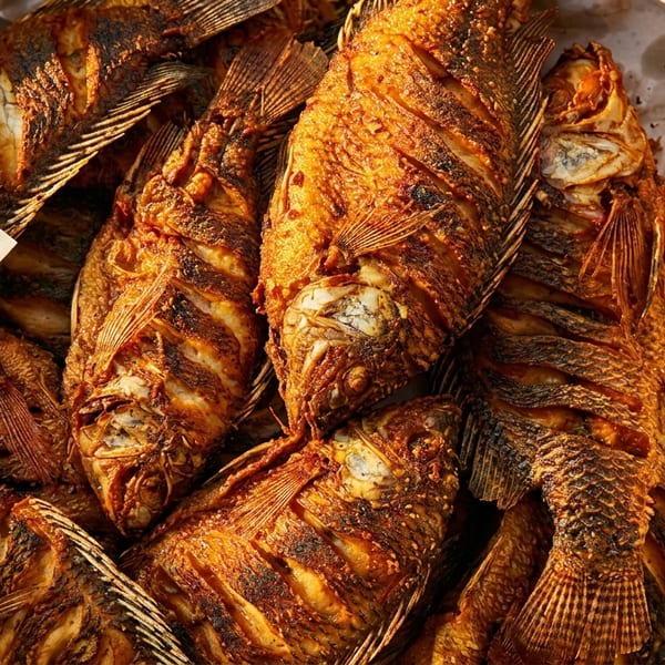 Close-up of several whole fried fish with crispy golden-brown skin, served on paper in a metal tray.